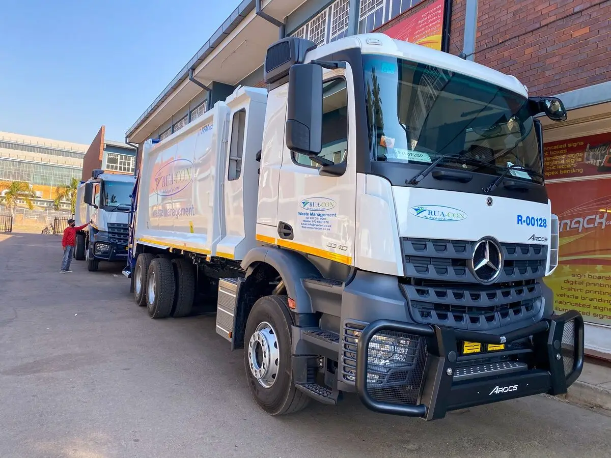 Rua-Con compactor truck parked outside a commercial building