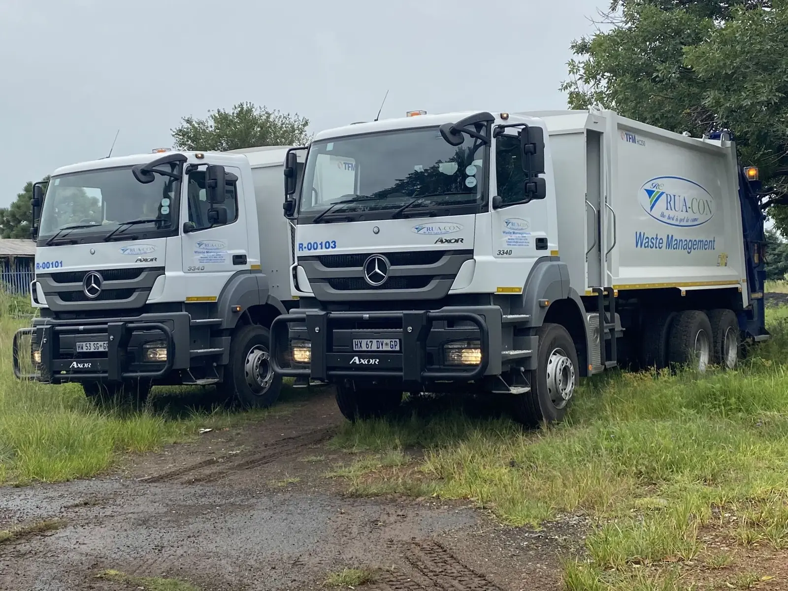Two Rua-Con refuse compactor trucks parked on grass