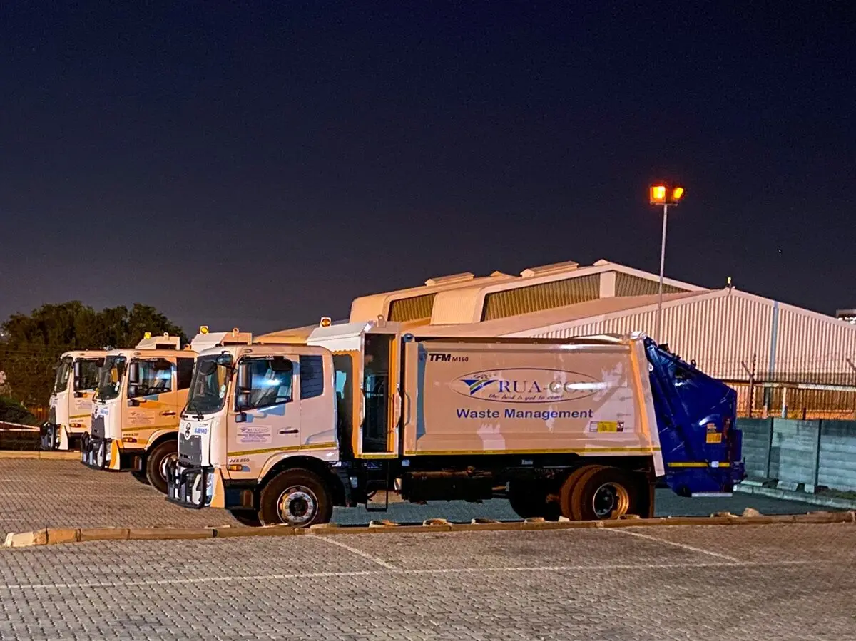 Row of Rua-Con compactor trucks at a depot at night