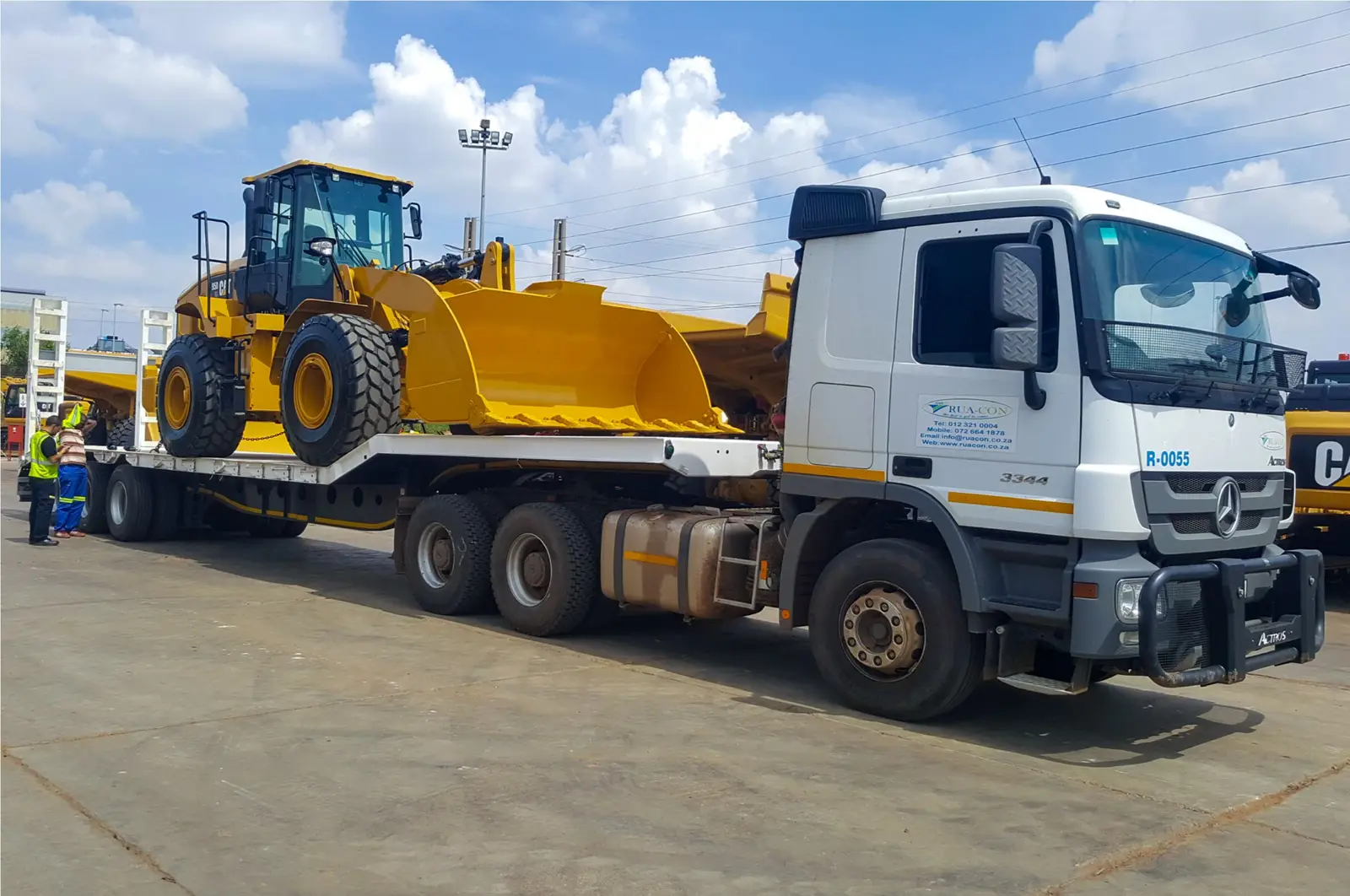 Rua-Con truck tractor and low-bed trailer transporting a yellow wheel loader